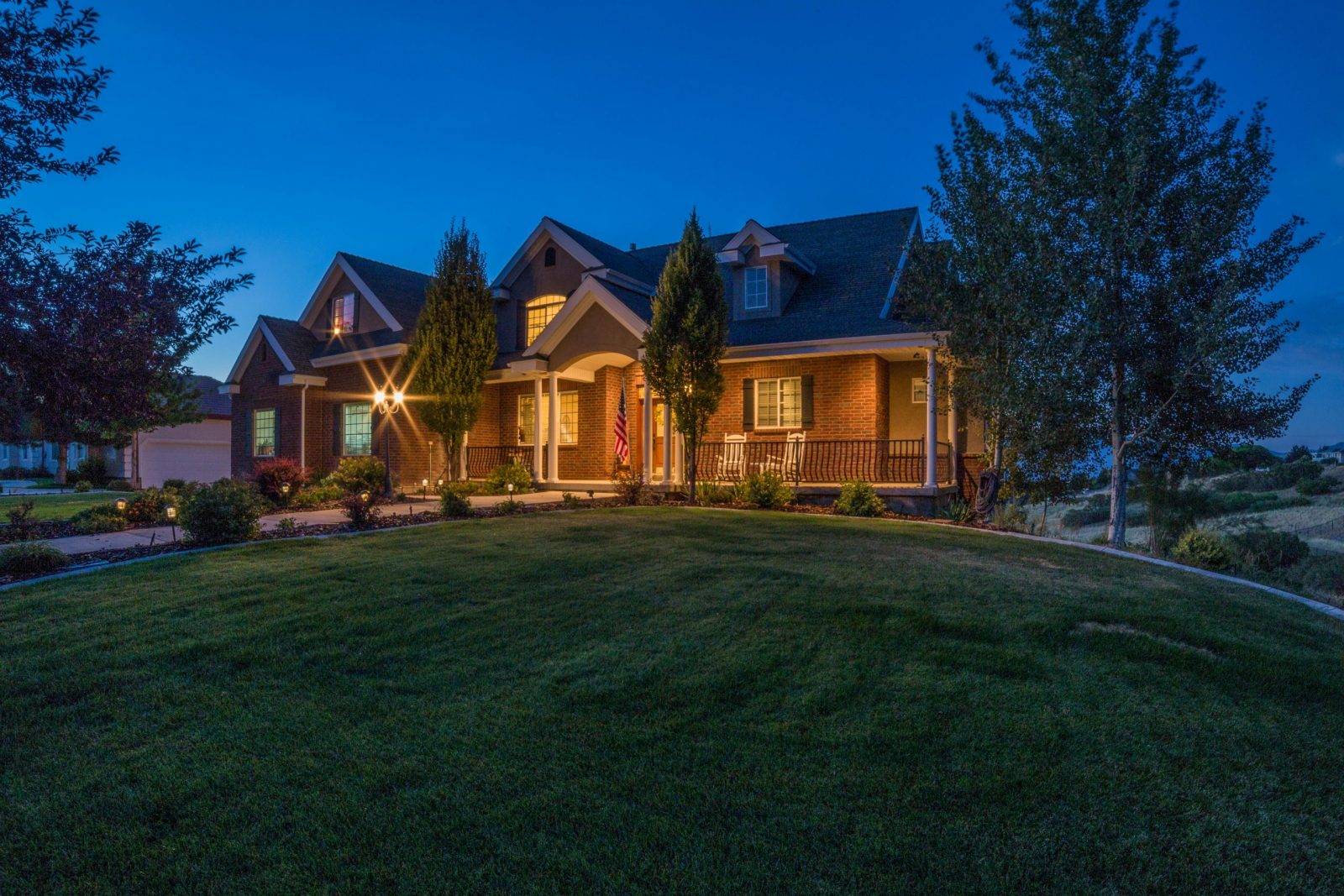 Beautiful country house with illuminated exterior at twilight, surrounded by greenery.